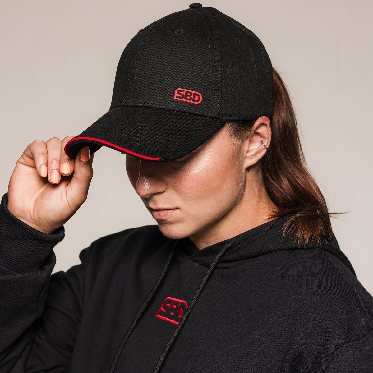 Black SBD Cap with red logo, front three-quarter view on an athlete