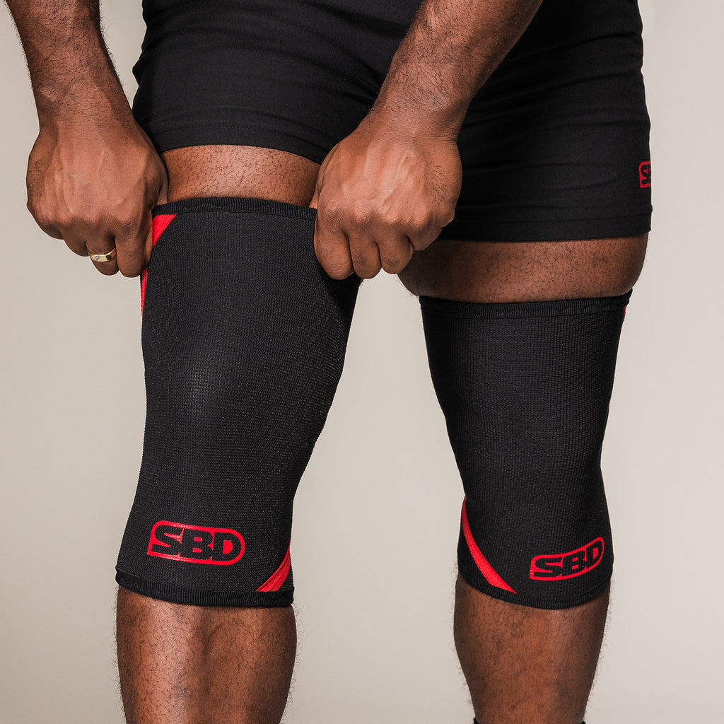 Black and red SBD Powerlifting Knee Sleeves, front view on an athlete