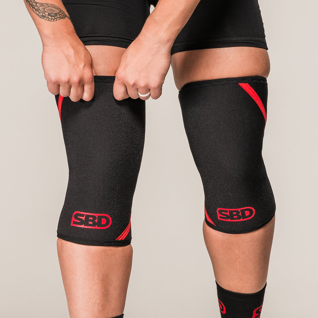 Black and red SBD Powerlifting Knee Sleeves, front view while being pulled into place