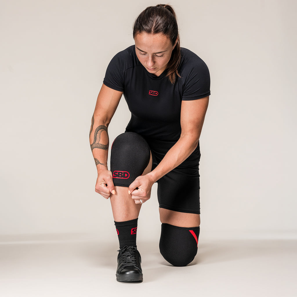 Athlete kneeling to adjust black and red SBD Powerlifting Knee Sleeves