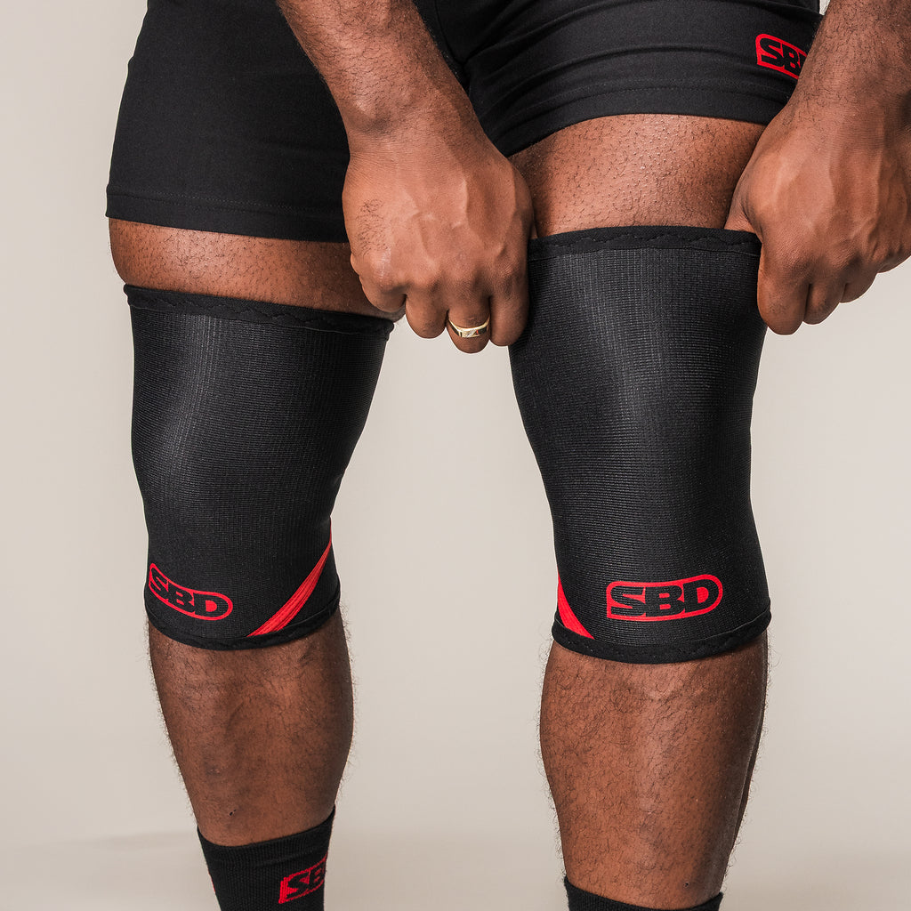 Black and red SBD Weightlifting Knee Sleeves, front view while being pulled into place