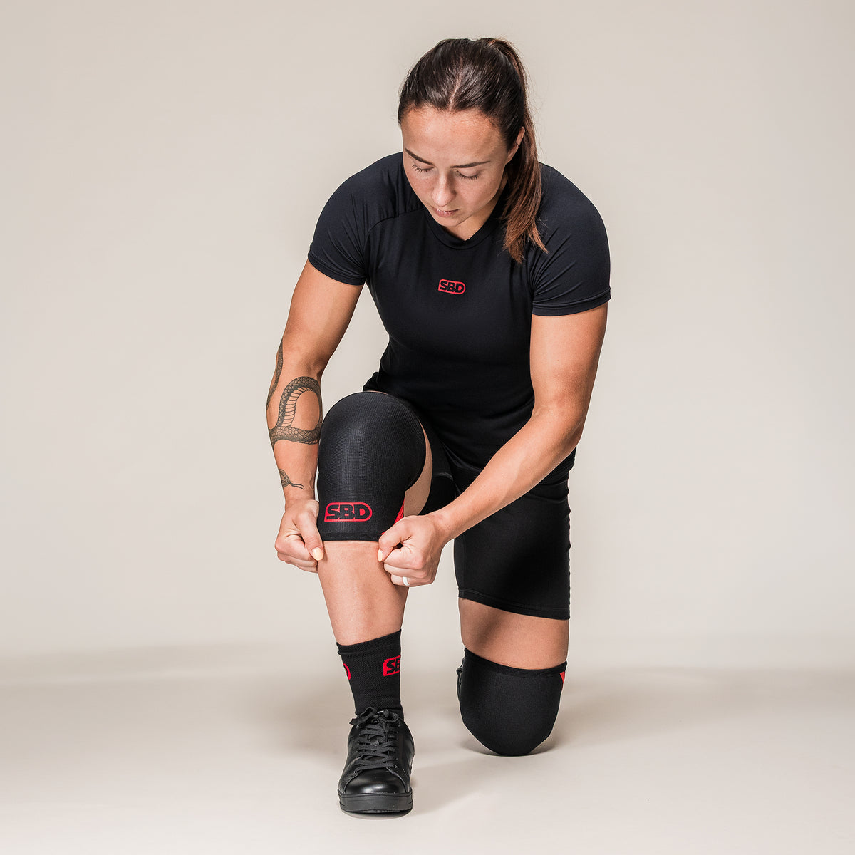 Athlete kneeling to adjust black and red SBD Weightlifting Knee Sleeves